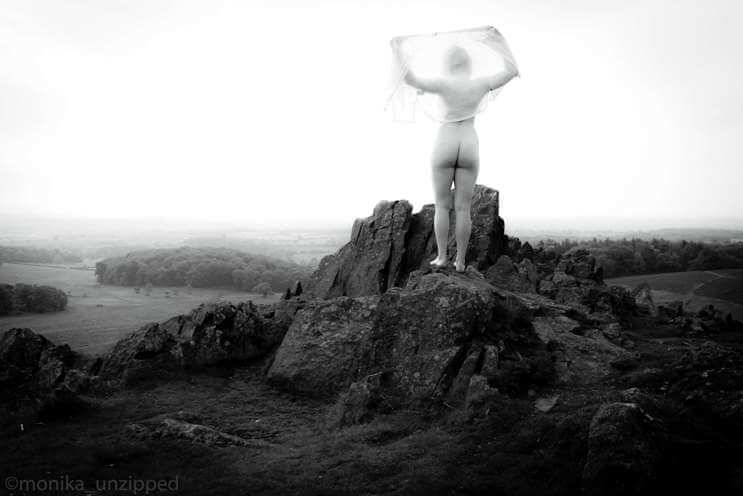 Monika standing naked on top of rocks looking down over the valley at Bradgate Park