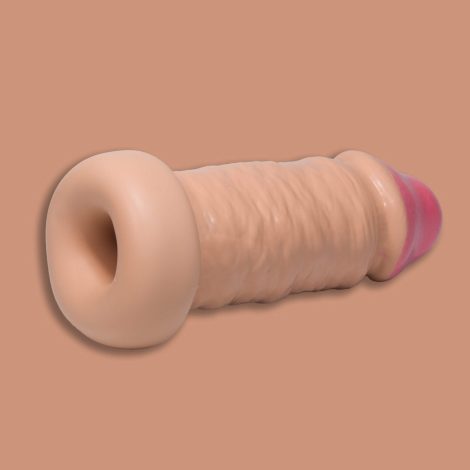 A Godemiche Silicone Penis extender with circumcised head. It is laying on its side and is partially rolled up and we can see up inside it. It is a cream colour and on a pinky/cream back ground