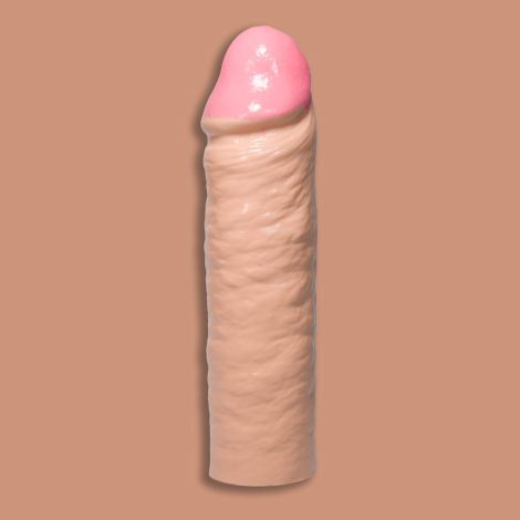 A Godemiche Silicone Penis extender with circumcised head. It is a cream colour and on a pinky/cream back ground