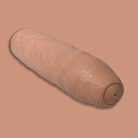 A Godemiche Silicone Penis extender with uncircumscised head. We can see the tip and the little hole in the top. It is a cream colour on a similar cream colour back ground