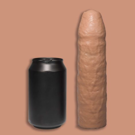 A Godemiche Silicone Dildo Penis extender with uncircumcised head next to can of soda. It is a cream colour and on a pinky/cream back ground